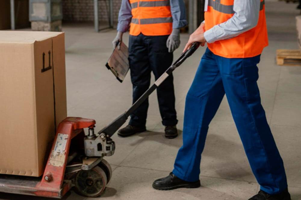 warehouse worker is using a pallet mover to transport boxes